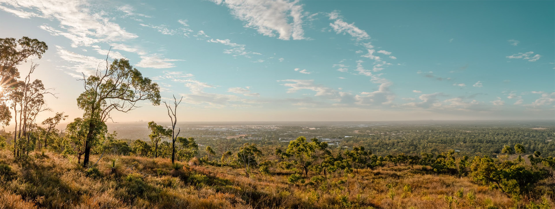 Panoramic view from the Perth Hills at sunrise – bushland, trails, and cityscape in the distance